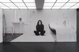 A black and white photo of an asian woman sitting in a museum installation