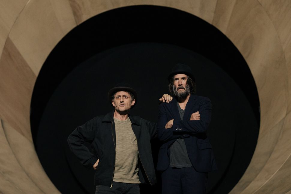 An image shows actors Alex Winter and Keanu Reeves standing side by side in bowler hats against the large circular wooden tunnel set of Waiting for Godot.