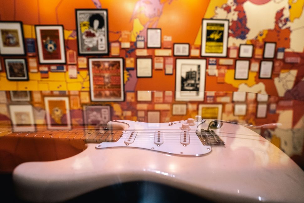 Jimi Hendrix's guitar laid flat in front of a wall of his performances at an exhibition at Seattle's Museum of Pop Culture