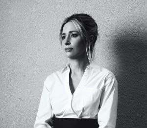 A black and white photo of a seated blonde woman wearing a black high-waisted skirt and a while button down shirt
