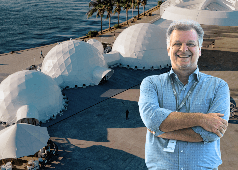 A portrait of a smiling man with his arms folded superimposed over an overhead shot of a waterfront plaza with three connected white domes